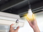 Power saving concept. Asia man changing compact-fluorescent (CFL) bulbs with new LED light bulb.